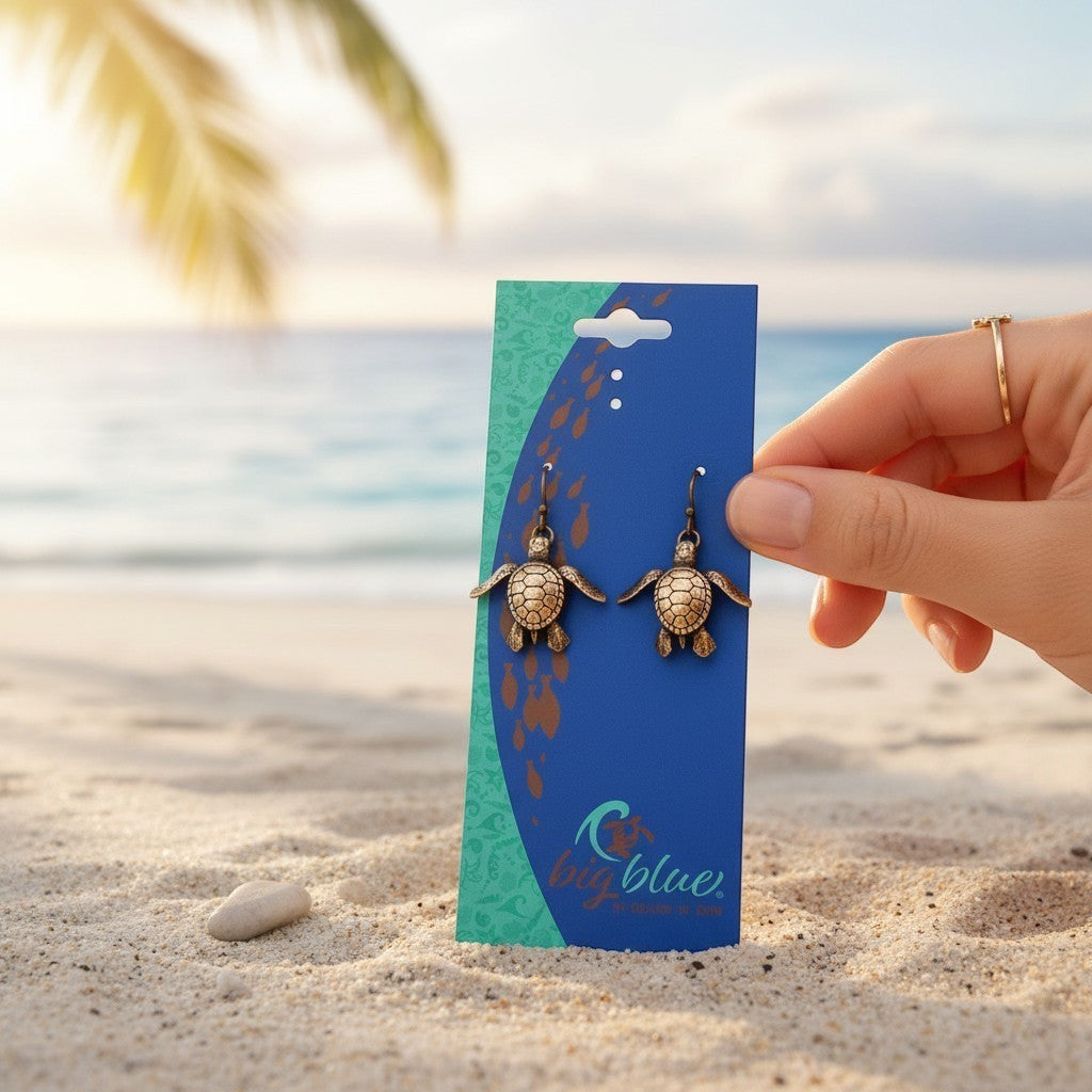 Big Blue by Roland St John bronze baby sea turtle drop earrings, detailed hatchling design, on display card on a beach.