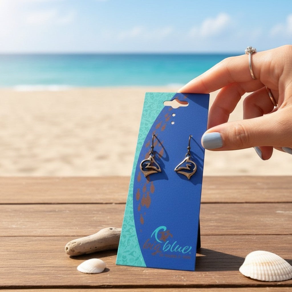 Big Blue by Roland St John bronze shark drop earrings with French hook ear wires, displayed on a blue card against a beach backdrop.