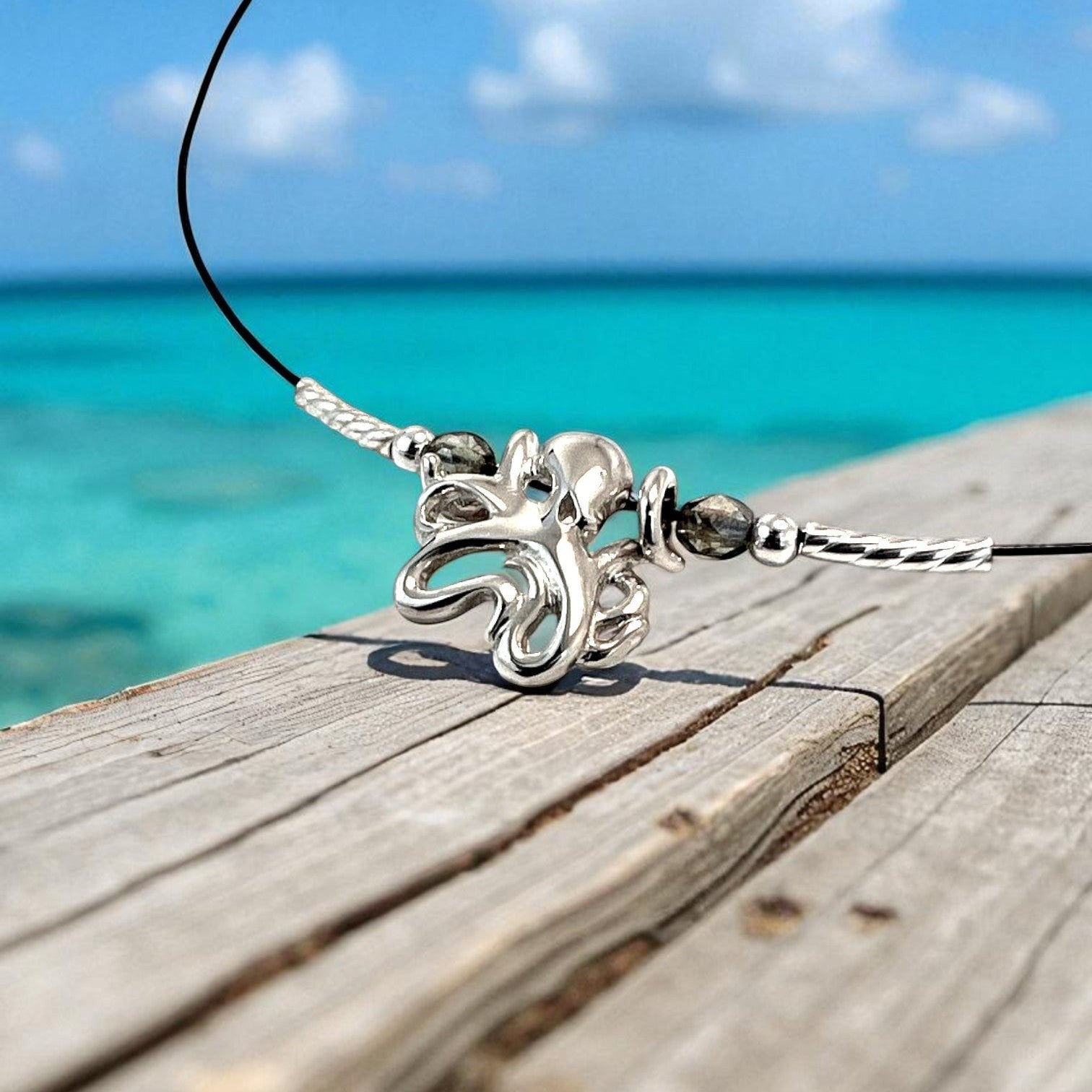 Big Blue by Roland St John sterling silver choker necklace with a mini octopus pendant and grey beads, set against a tropical ocean backdrop.