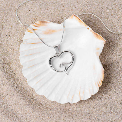 Big Blue by Roland St John sterling silver ocean wave heart pendant on snake chain, resting on a large seashell on sand.