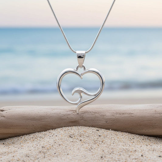 Big Blue by Roland St John sterling silver heart wave pendant necklace on snake chain, set on a beach with ocean background.