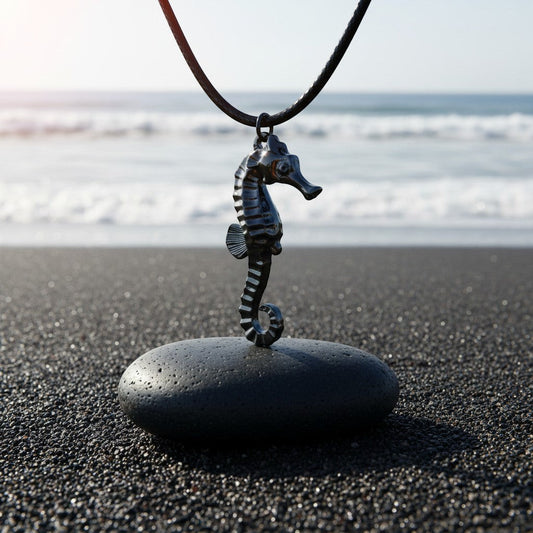 Big Blue by Roland St John jet black hematite finish seahorse pendant on black cotton cord, displayed on a dark stone on a black sand beach.
