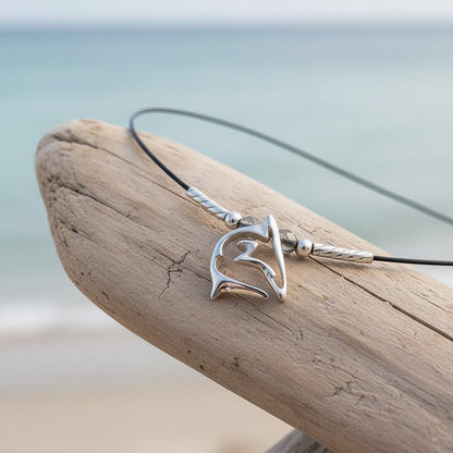 Big Blue by Roland St John sterling silver shark pendant necklace on black cable wire, set on driftwood with ocean background.