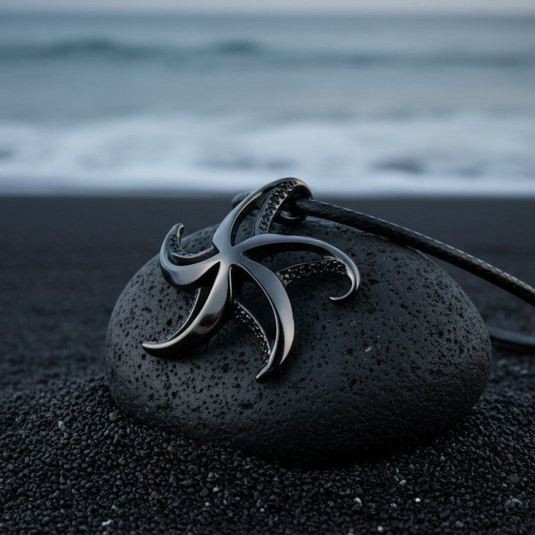 Big Blue by Roland St John starfish necklace with jet black finish on a black cord, resting on a dark stone on black sand.