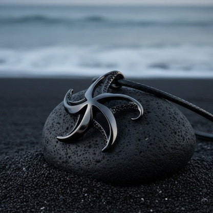 Big Blue by Roland St John starfish necklace with jet black finish on a black cord, resting on a dark stone on black sand.