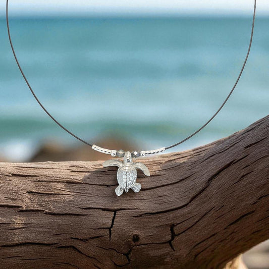 Big Blue by Roland St John sterling silver sea turtle choker necklace on cable wire with beaded accents, set against a blurred beach background.