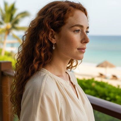Big Blue by Roland St John bronze whale shark drop earrings on a woman with red curly hair by the ocean.