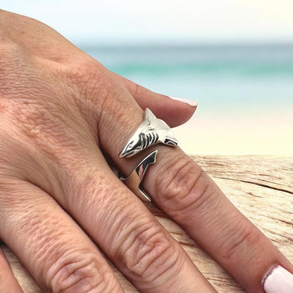 Big Blue by Roland St John sterling silver adjustable shark ring, detailed and realistic design, worn on a finger with a beach and ocean in the background.