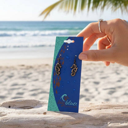 Big Blue by Roland St John bronze seahorse drop earrings with French ear wires, displayed on a card against a beach backdrop.
