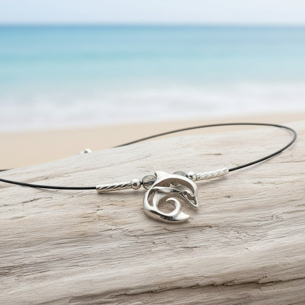 Big Blue by Roland St John sterling silver choker necklace with a miniature dolphin pendant on a black cord, set against a beach background.