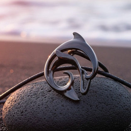 Big Blue by Roland St John jet black dolphin pendant necklace on black cord, resting on a dark stone at the beach.