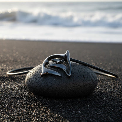 Big Blue by Roland St John "Frenzy" shark necklace in jet black finish on black cord, resting on a dark stone on a black sand beach.