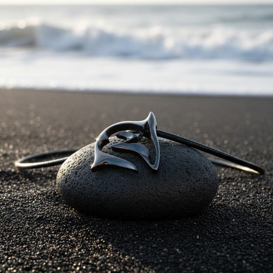 Big Blue by Roland St John "Frenzy" shark necklace in jet black finish on black cord, resting on a dark stone on a black sand beach.