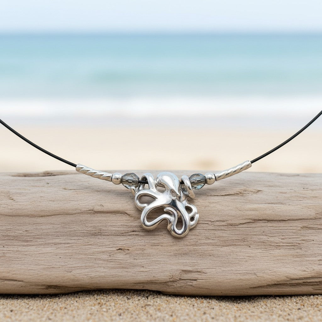 Big Blue by Roland St John sterling silver choker necklace with a mini octopus pendant and grey beads, set on a driftwood piece on a beach.