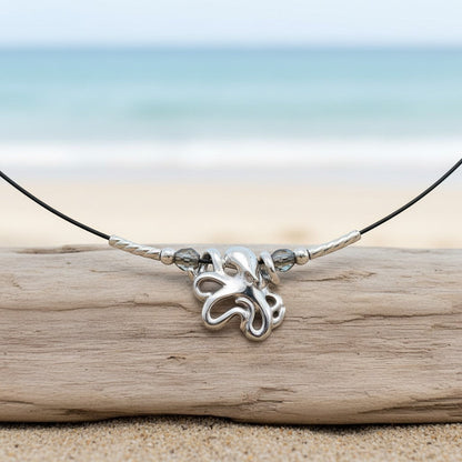 Big Blue by Roland St John sterling silver choker necklace with a mini octopus pendant and grey beads, set on a driftwood piece on a beach.