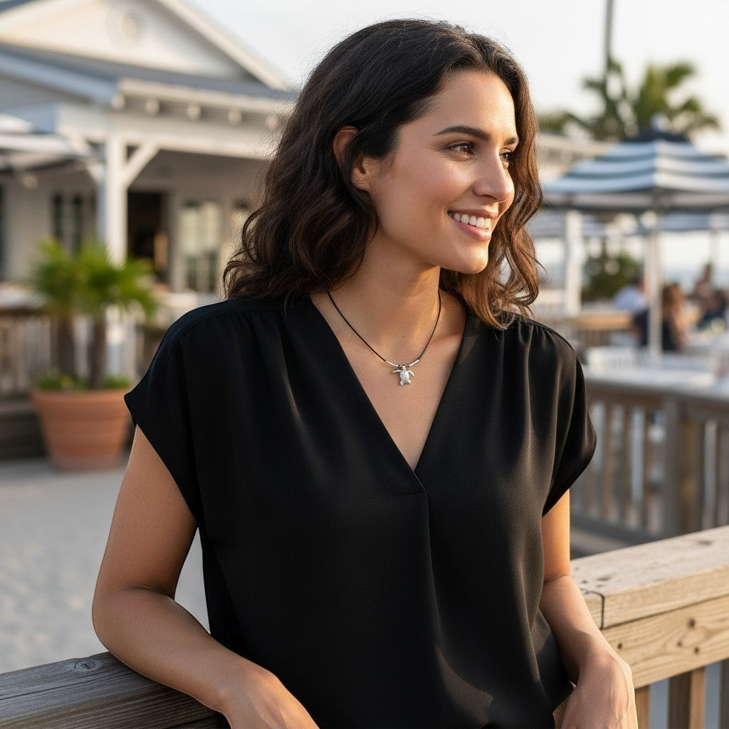 Big Blue by Roland St John sterling silver sea turtle choker necklace on a black cable wire, worn by a smiling woman on a boardwalk.