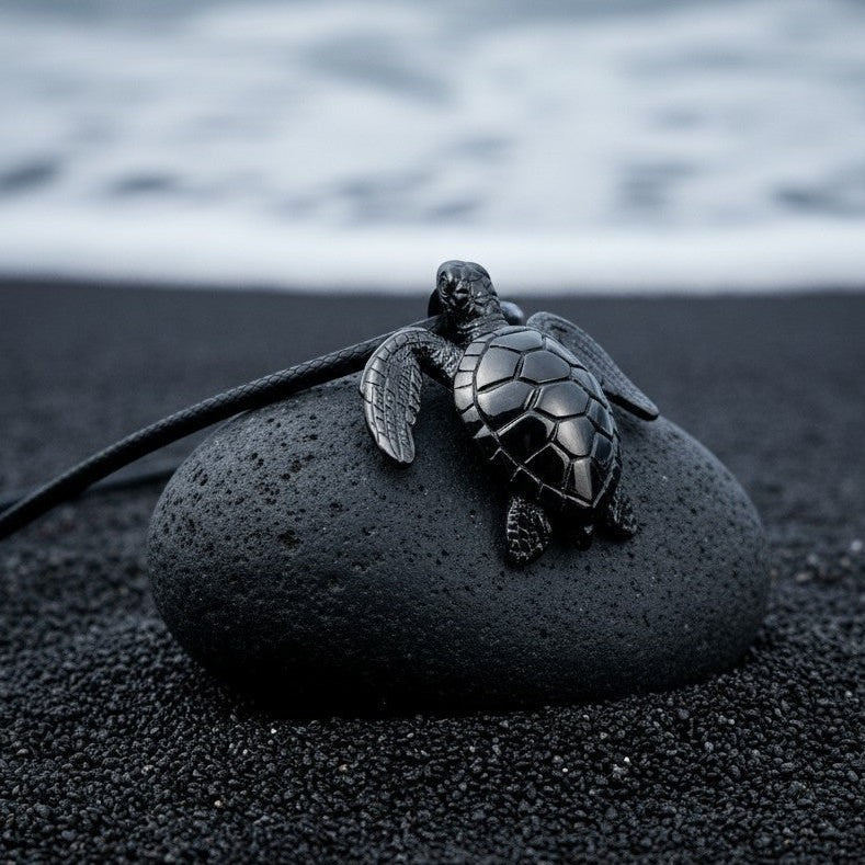 Big Blue by Roland St John sea turtle pendant in jet black finish on a dark stone on black sand beach.
