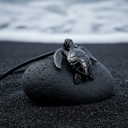Big Blue by Roland St John sea turtle pendant in jet black finish on a dark stone on black sand beach.