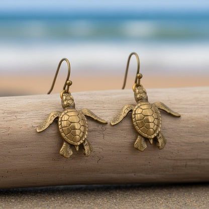 Big Blue by Roland St John bronze baby sea turtle drop earrings with detailed shells and flippers, on a beach setting.