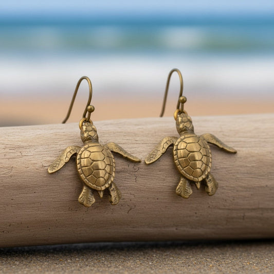 Big Blue by Roland St John bronze baby sea turtle drop earrings with detailed shells and flippers, on a beach setting.