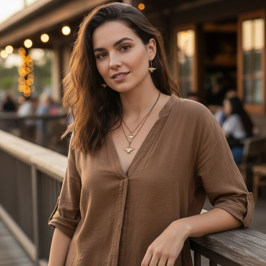 Bronze manta ray drop earrings and layered necklace on a woman wearing a brown shirt. Big Blue by Roland St John.