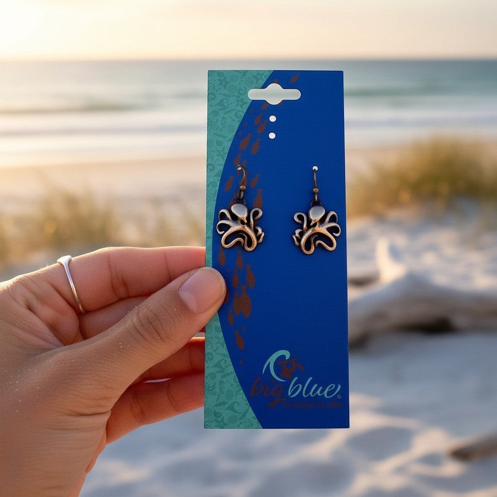 Big Blue by Roland St John bronze octopus drop earrings with secure ear wires, displayed on a card against a beach sunset.