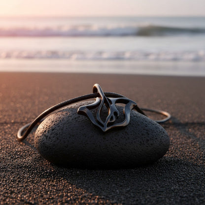 Big Blue by Roland St John jet black finish stingray pendant necklace on a dark stone at the beach.