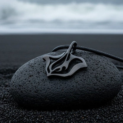 Big Blue by Roland St John jet black stingray pendant necklace on a dark stone on black sand.
