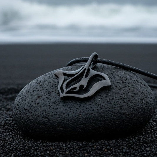 Big Blue by Roland St John jet black stingray pendant necklace on a dark stone on black sand.