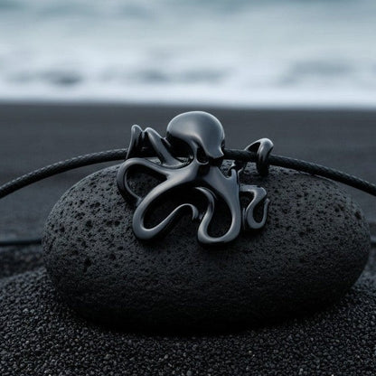 Big Blue by Roland St John Leggs octopus pendant necklace in jet black finish on a black cord, resting on a dark stone on black sand.
