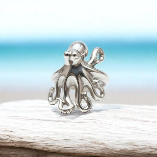 Big Blue by Roland St John sterling silver octopus ring with detailed tentacles, adjustable fit, on driftwood with beach background.