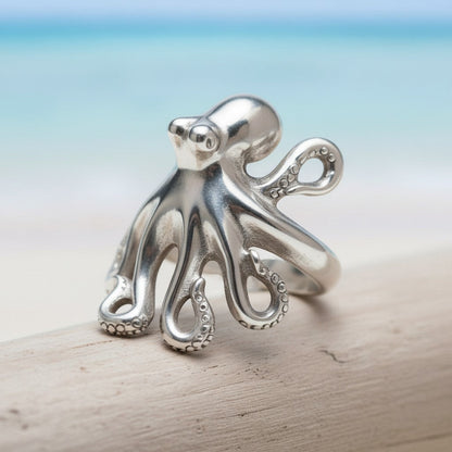 Big Blue by Roland St John sterling silver octopus ring with detailed tentacles, adjustable fit, on a wooden surface with a beach background.