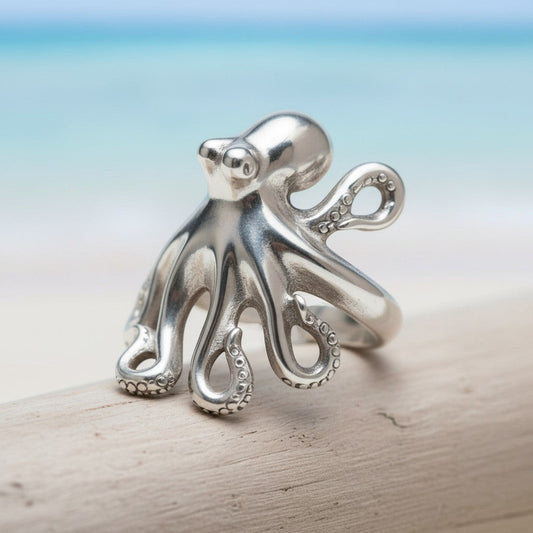 Big Blue by Roland St John sterling silver octopus ring with detailed tentacles, adjustable fit, on a wooden surface with a beach background.