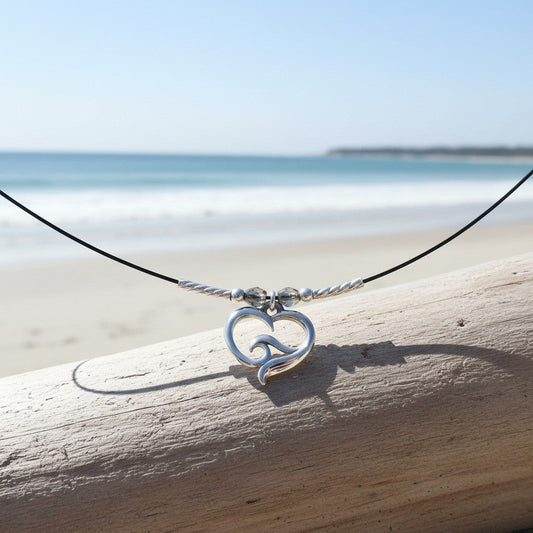 Big Blue by Roland St John sterling silver ocean wave heart choker necklace with grey beads on a black cord, set against a beach background.